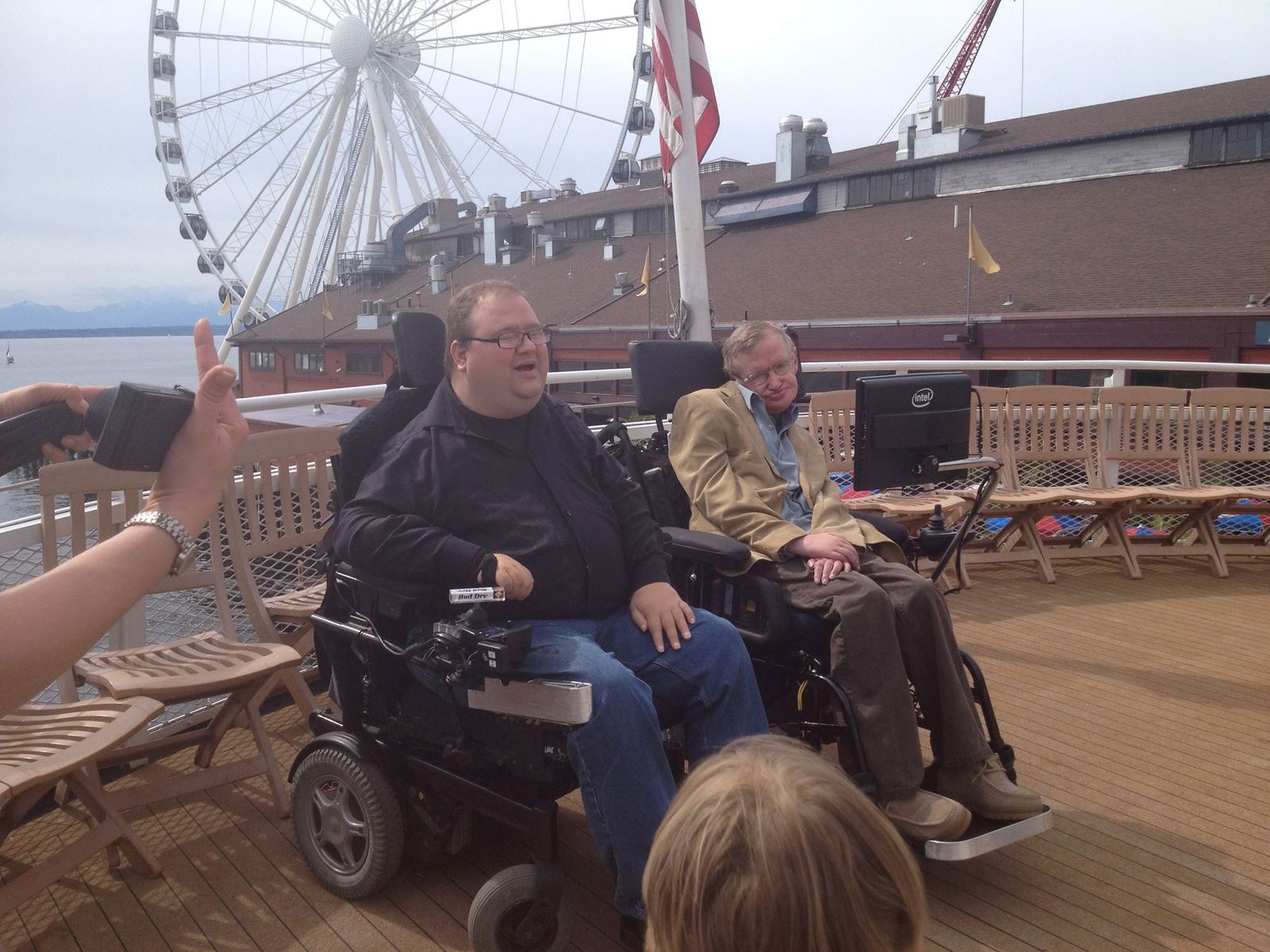 Pete Denman and Stephen Hawking together on the Seattle waterfront near the Great Wheel, Stephen's monitor arm visible on his chair.